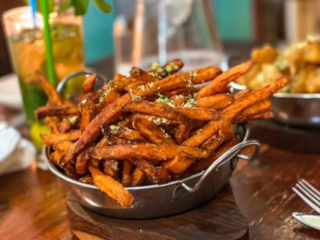 Sweet potato fries in a steel bowl, mojitos behind