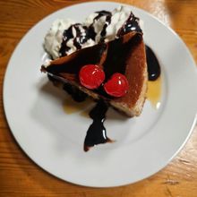 A slice of dessert with chocolate sauce and cherries