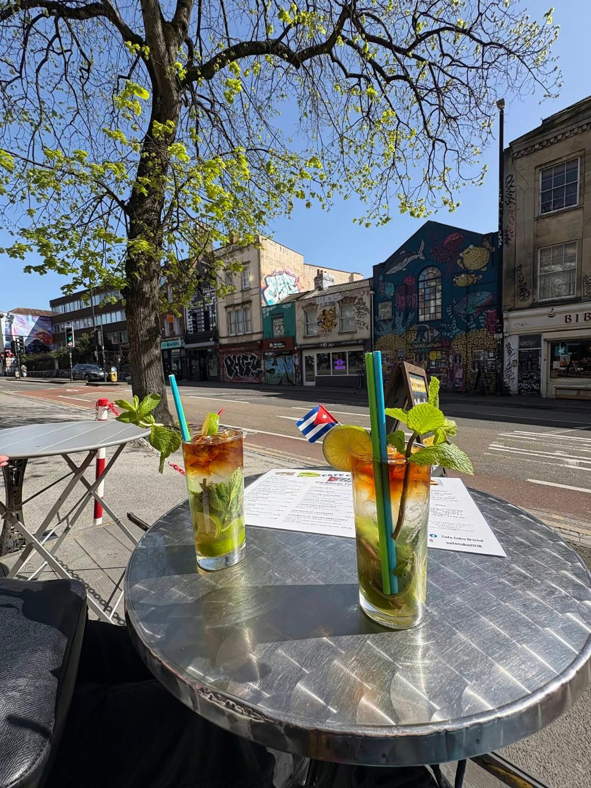 Two mojitos on a steel café table on Stokes Croft, a Cuban flag pick in one