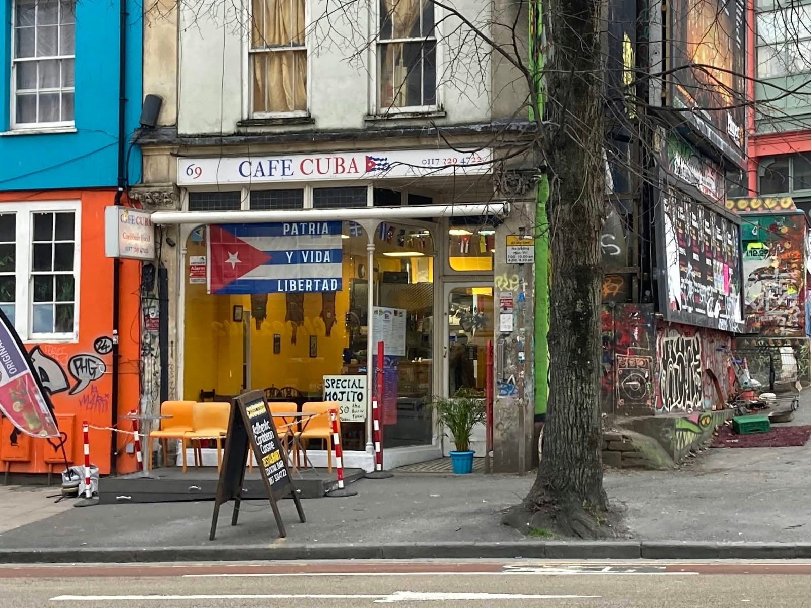 The Cafe Cuba shopfront at 69 Stokes Croft, a 'Patria y Vida' flag in the window and orange chairs outside